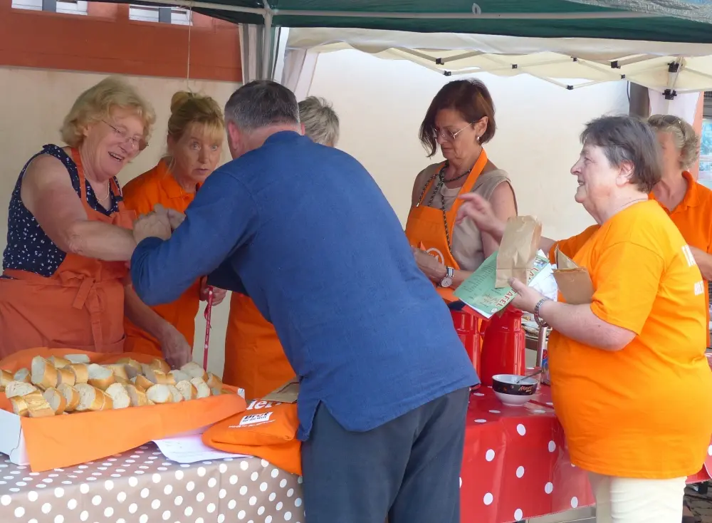 Ehrenamtliche der Haßfurter Tafel in orangefarbenen Schürzen und T-Shirts geben beim Tafel-Jubiläum Brot an einen Besucher aus