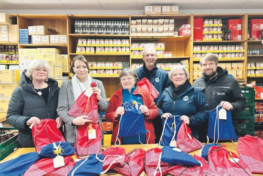 Tafel-Team und Gäste im Tafelladen vor Regalen mit Lebensmitteln, in den Händen rote und blaue Geschenkbeutel