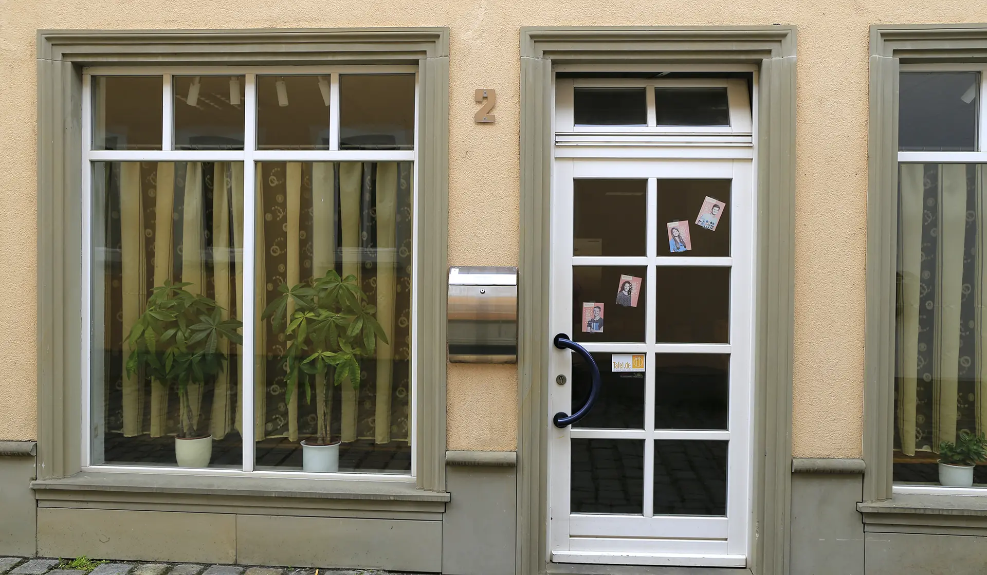 Eingang des Tafelladens Haßfurt: weiße Tür mit Sprossenfenster an einer gelben Hausfassade