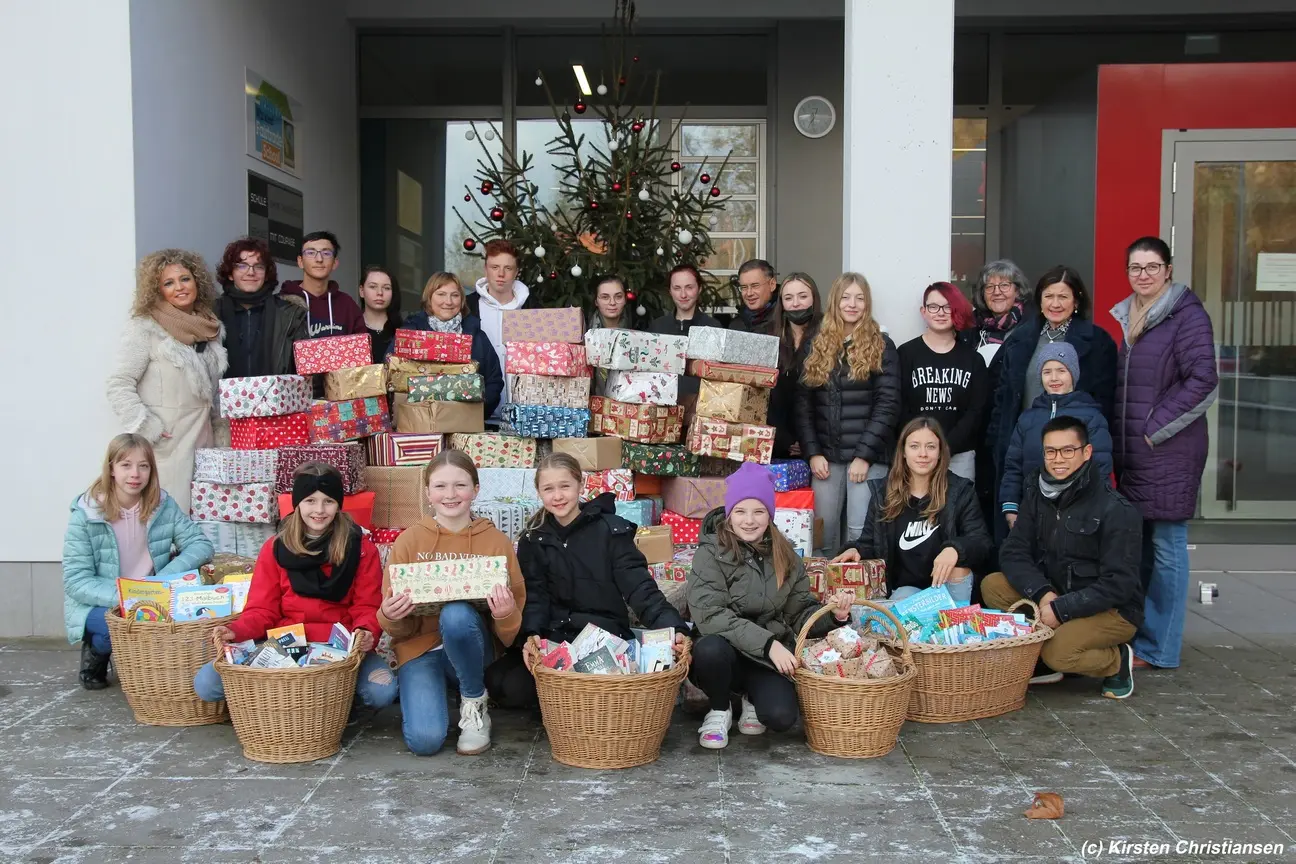 Kinder und Jugendliche mit Körben voller Weihnachtspäckchen vor einem Christbaum